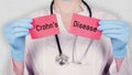 Closeup, hands in blue medical gloves hold and tear red paper card with an inscription Crohns Disease. doctor dressed in