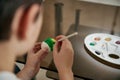 Closeup of hands of a boy holding an egg and decorating it with a green paint and paintbrush. Celebration Easter concept