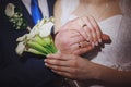 Closeup of hands of bridal couple with wedding rings. Bride holds wedding bouquet of white flowers