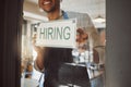 closeup on hands of business owner hanging a hiring sign. Small business owner advertising hiring for his shop