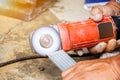 Hands of laborer holding electric angle grinder working chamfer at construction site with sun flare background