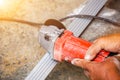 Hands of laborer holding electric angle grinder working cutting aluminium lumber at construction site with sun flare Royalty Free Stock Photo