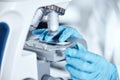 Closeup of the hands of one young woman wearing a labcoat and gloves and looking at medical samples on a microscope in