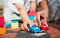 Closeup hands playing with fun toys, cars and building blocks in a home living room. Parent bonding, having fun and