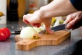 Closeup of the hands of a woman cook slicing onion on a wooden board.