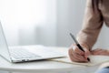 Closeup hands young asian woman writing on notebook for planning working and using laptop computer on desk. Royalty Free Stock Photo