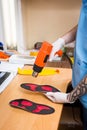 Closeup Hands of young man with tattoo in workshop dressed in blue uniform make individual orthopedic insoles. The instrument uses