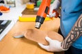 Closeup Hands of young man with tattoo in workshop dressed in blue uniform make individual orthopedic insoles. The instrument uses