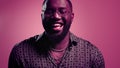 Happy afro guy laughing indoors. Male person giggling on pink background Royalty Free Stock Photo