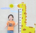 Closeup happy asian kid stand for measure height with cute cartoon at the marble stone wall textured background Royalty Free Stock Photo