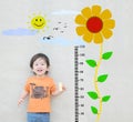 Closeup happy asian kid stand for measure height with cute cartoon sunflower at the marble stone wall textured background Royalty Free Stock Photo