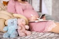 Closeup happy future mother admiring x ray ultrasound photo writing paper diary relaxing on bed. two bear toys