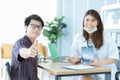 Closeup of happy young Asian male patieent with casual clothes is showing thumbs up while sitting with beautiful female doctor Royalty Free Stock Photo