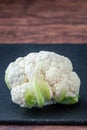 Closeup of head of cauliflower on a black cutting board on a wood table Royalty Free Stock Photo