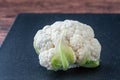 Closeup of head of cauliflower on a black cutting board on a wood table Royalty Free Stock Photo