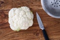 Closeup of head of cauliflower on a rustic wood cutting board, paring knife, colander Royalty Free Stock Photo