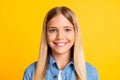 Closeup headshot of nice friendly schoolgirl with blonde hair wearing denim shirt smiling isolated on bright yellow