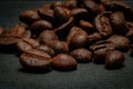 Closeup of a heap of coffee beans on a dark gray surface.