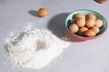 Closeup of a heap of wheat flour next to a bowl filled with brown eggs on a table