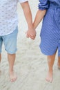 Closeup holding hands of happy couple walking barefoot on sand. Royalty Free Stock Photo