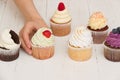 Closeup of homemade vanilla, blueberyy, lemon, chocolate cupcakes and woman`s  hand on white retro wooden background Royalty Free Stock Photo