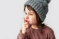 Closeup horizontal image of cute beautiful little girl in the winter warm gray hat, wearing sweater and showing silent gesture,