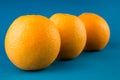 Closeup of a horizontal row of three vibrant orange oranges on light blue background