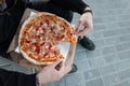 Closeup hot delicious pizza with sausage with cheese and tomatoes in the hands of a man in black stylish clothes. Royalty Free Stock Photo