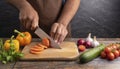 Closeup on human hands cutting vegetables on wooden cutting board with knife