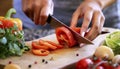 Closeup on human hands cutting vegetables on wooden cutting board with knife