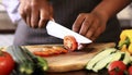 Closeup on human hands cutting vegetables on wooden cutting board with knife