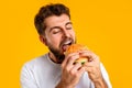 Closeup of hungry man savoring a tasty hamburger, yellow background Royalty Free Stock Photo