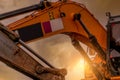 Closeup hydraulic piston arm of dirty backhoe at construction site. Yellow excavator parked at construction site against sunset