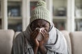 Closeup of ill african american man covered in blanket sneezing Royalty Free Stock Photo