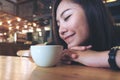 Closeup image of Asian woman sit with chin resting on her hands and closing her eyes smelling hot coffee on wooden table with feel Royalty Free Stock Photo