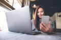 A beautiful Asian woman holding and looking at mobile phone while using laptop in cafe Royalty Free Stock Photo