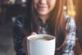 Closeup image of a beautiful Asian woman holding and showing a white mug while drinking hot coffee with feeling good Royalty Free Stock Photo