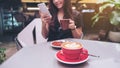 Closeup image of a beautiful Asian woman holding and using smartphone while drinking coffee with latte coffee cup on glass table Royalty Free Stock Photo