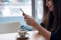 A beautiful Asian woman with smiley face holding and using smart phone with coffee cup on wooden table in cafe Royalty Free Stock Photo