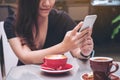 Closeup image of a beautiful Asian woman with smiley face holding and using smart phone with coffee cups on glass table Royalty Free Stock Photo