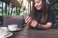 Closeup image of a beautiful Asian woman with smiley face holding and using smart phone with coffee cups on wooden table Royalty Free Stock Photo