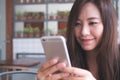 Closeup image of a beautiful Asian woman with smiley face holding and using smart phone while drinking hot coffee on wooden table Royalty Free Stock Photo