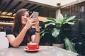 A beautiful Asian woman with smiley face holding and using smart phone with a red coffee cup on glass table in modern cafe Royalty Free Stock Photo