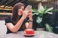 A beautiful Asian woman with smiley face holding and using smart phone with a red coffee cup on glass table in modern cafe Royalty Free Stock Photo