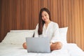 A beautiful asian woman using and working on laptop computer while sitting on a white cozy bed at home Royalty Free Stock Photo