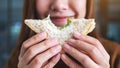 A beautiful woman holding and biting a piece of whole wheat sandwich