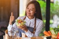 A beautiful young asian female chef making and showing thumbs up hand sign while cooking and holding fresh mixed Royalty Free Stock Photo
