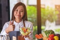 A beautiful young asian female chef making and showing thumbs up hand sign while cooking and holding fresh mixed Royalty Free Stock Photo