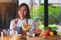 A beautiful young asian female chef making and showing thumbs up hand sign while cooking and holding fresh mixed Royalty Free Stock Photo