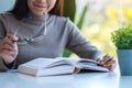 A beautiful young asian woman holding eye glasses while reading book Royalty Free Stock Photo